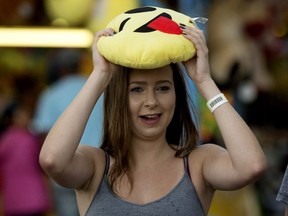 A woman hides from the rain under a stuffed emoji as she heads for cover at K-Days, in Edmonton on Wednesday July 27, 2016.
