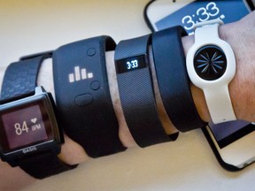 FILE - In this Dec. 15, 2014 file photo, fitness trackers, from left, Basis Peak, Adidas Fit Smart, Fitbit Charge, Sony SmartBand, and Jawbone Move, are posed for a photo next to an iPhone, in New York. Sales of fitness trackers are climbing, and the biggest maker of the gadgets, Fitbit, made a splashy debut on the stock market Thursday, June 18, 2015.