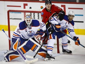 Edmonton Oilers goalie Jonas Gustavsson, left, of Sweden, and Darnell Nurse, right, pin Calgary Flames' Matthew Tkachuk, during second period pre-season NHL split-squad hockey action in Calgary, Monday, Sept. 26, 2016.