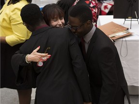 Presiding official Elexis Schloss hugs twin brothers Joseph Jr. (left) and Emmanuel Jo-Daria (right) after they received their citizenship papers during a ceremony at City Hall on Friday.