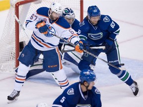Edmonton Oilers' Benoit Pouliot, left, tips the puck in front of Vancouver Canucks' Philip Larsen, of Denmark, but is stopped by goalie Ryan Miller, back, during the second period of an NHL hockey game in Vancouver, B.C., on Friday October 28, 2016.