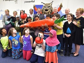 Grade 3 Rundle School students, some of them trying to eat the carrot, pose with officials after the Edmonton Oilers Community Foundation announced a $750,000 donation to E4C's school snack program on Nov. 24, 2016.