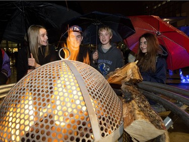 Visitors to the Holiday Light Up in Churchill Square huddle under umbrellas and warm up beside a fire, in Edmonton on Saturday Nov. 12, 2016.