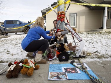 Two women pay their respects at a memorial in front of the home where three bodies were discovered on Monday in Spruce Grove, Alta., on Tuesday, Dec. 20, 2016.