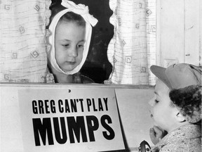 FILE - In this Jan. 16, 1957 file photo, Jon Douglas, 6, right, visits his friend, Greg Cox, standing behind a sign warning he has mumps, on the door of his home in Altamont, Ill. Fifty years ago, mumps was once a childhood rite of passage of puffy cheeks and swollen jaws. That all changed with the arrival of a vaccine in the late 1960s, and mumps nearly disappeared. But in 2017, the U.S. is in the midst of one of the largest surges in decades.