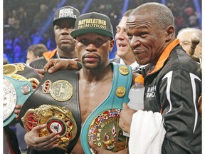 In this May 2, 2015 file photo, Floyd Mayweather Jr., left, poses with his champion's belts and his father, head trainer Floyd Mayweather Sr., after his victory over Manny Pacquiao in a welterweight title fight in Las Vegas. Mayweather is coming out of retirement to fight mixed martial artist Conor McGregor. (AP Photo)