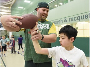 Edmonton Eskimo offensive lineman Justin Sorensen teaches I.V. Macklin Public School student Junseo Koh how to throw a football during a free football camp at the Eastlink Centre on Tuesday April 11, 2017 in Grande Prairie, Alta. The Eskimos will hold their annual mini-camp in Las Vegas this year.