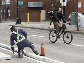 A cyclist passes as workers with Concrete Inc., install lanes for the permanent downtown bike lane system along 100 Avenue near 104 Street in Edmonton on Monday, May 1, 2017.