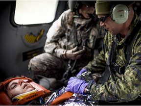 Cpl. Jason Flegel (right), of 2 Field Ambulance, and Sgt. Becky Himmel (centre), a medic from the United States Army, tend to a simulated injured soldier mid-flight inside of a UH-60 Black Hawk helicopter during Exercise Maple Resolve, the largest and most comprehensive Canadian Army training event each year, held in Wainwright.