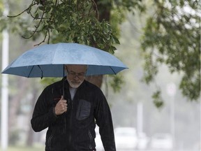 A man walks in heavy rain with his umbrella near 98 Street and 88 Avenue in Edmonton.