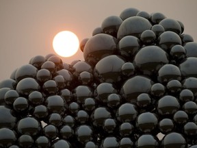 The Sun, partially obscured by smoke from the B.C. forest fires, begins to set behind the Talus Dome sculpture, in Edmonton Wednesday July 19, 2017.