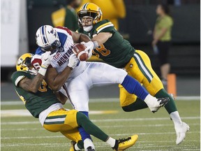 Montreal Alouettes' Nik Lewis (8) is tackled by Edmonton Eskimos' Adam Konar (38) and Garry Peters (34) during second half CFL action in Edmonton on Friday, June 30, 2017.