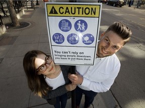 Morgan Wedderspoon and Chris Gusen pose for a photo with a sign from their art project "Jane Jacobs on Jasper," near Jasper Avenue and 104 Street in Edmonton Monday, July 17, 2017. The duo hope the fake warning signs they posted will start a conversation about what creates a great downtown.