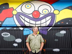 Fringe Theatre artistic director Murray Utas poses in front of a mural created by artists at iHuman Youth Society outside the Arts Barns in Old Strathcona.