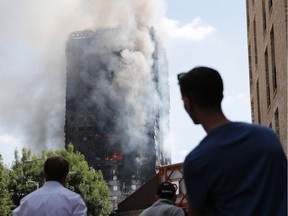 This file photo taken on June 14, 2017 shows pedestrians looking up towards Grenfell Tower, a residential block of flats in west London, as firefighters continue to control a fire that engulfed the building in the early hours of the morning.