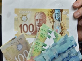 Const. Zachary Jansen holds up counterfeit and altered currency in Edmonton, Friday, November 25, 2016