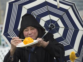 Elvie Paras eats a mango on a stick from the Guatemala Pavilion while holding her umbrella. The last day of the three-day Heritage Festival at Hawrelak Park was dampened by  rainy weather on Sunday, Aug. 7, 2017.