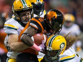 Edmonton Eskimos' Adam Konar, left, and Aaron Grymes, right, tackle B.C. Lions' Chris Rainey (2) during CFL action in Vancouver on October 21, 2017.