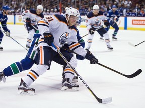 Edmonton Oilers' Drake Caggiula, front, skates towards the net with the puck while being checked by Vancouver Canucks' Ben Hutton during the third period of a preseason NHL hockey game in Vancouver, B.C., on Saturday September 30, 2017.