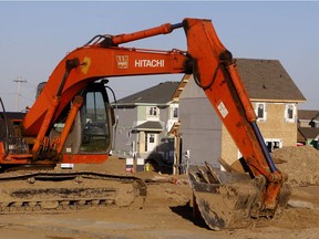 A large excavator sits idle with new and under-construction houses in the background in west Edmonton.