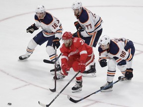 Detroit Red Wings defenseman Nick Jensen (3) reaches for the puck while defended by Edmonton Oilers center Ryan Strome (18), defenseman Oscar Klefbom (77) and right wing Jesse Puljujarvi (98) during the third period of an NHL hockey game, Wednesday, Nov. 22, 2017, in Detroit.