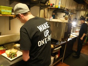 Nick Thompson, cook at the Black Tomato restaurant, works in the kitchen wearing a "wake up Ontario" slogan.   Owner Peter Besserer is closing the Black Tomato at the end of the month after 23 years in business. He blames the higher minimum wage which he says will cost him $80,000 a year for his 17 employees Besserer has made up 'Wake Up Ontario' tshirts for his staff to wear and is putting up banners Tuesday to make his point.