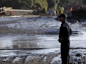 A California Highway Patrol officer stands in front of a road damaged from storms in Montecito, Calif., Thursday, Jan. 11, 2018. Rescue workers slogged through knee-deep ooze and used long poles to probe for bodies Thursday as the search dragged on for victims of the mudslides that slammed this wealthy coastal town.