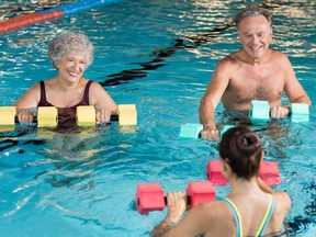 Senior couple in training session of aqua aerobics using dumbbells in swimming pool. Mature man and old woman practicing aqua fitness together. Healthy and fit senior couple enjoying their retirement in aqua aerobics training.