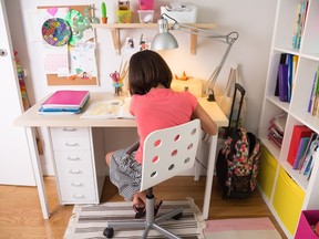 School girl doing homework at home in her desk. Back view.