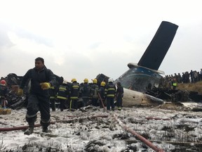 Nepalese rescuers stand near a passenger plane from Bangladesh that crashed at the airport in Kathmandu, Nepal, Monday, March 12, 2018.