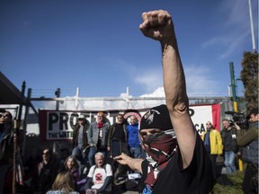 A protester raises his fist as others block a gate outside the Kinder Morgan site in Burnaby, B.C., on Saturday, March 17, 2018. Approximately 30 people who blockaded an entrance, defying a court order, were arrested while protesting the Kinder Morgan Trans Mountain pipeline expansion.