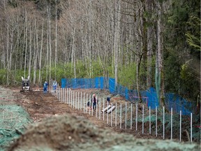 Workers set poles for a new fence under construction at Kinder Morgan's facility in preparation for the expansion of the Trans Mountain Pipeline, in Burnaby, B.C., on April 9, 2018.