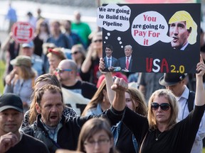 A woman holds a sign bearing photographs of Prime Minister Justin Trudeau and U.S. President Donald Trump during a protest against the Kinder Morgan Trans Mountain Pipeline expansion on May 29, 2018.