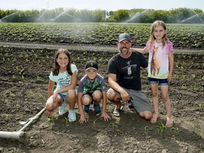 Aaron Herbert with his children (left to right) Evie, Layne and Carly in their corn and potato field located in northeast Edmonton on May 25, 2018.
