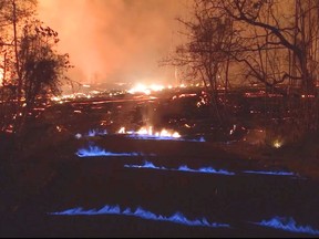 This photo from video from the U.S. Geological Survey shows blue burning flames of methane gas erupting through cracks on Kahukai Street in the Leilani Estates neighborhood of Pahoa on the island of Hawaii during the overnight hours of Wednesday, May 23, 2018. When lava buries plants and shrubs, methane gas is produced as a byproduct of burning vegetation. Methane gas can seep into subsurface voids and explode when heated, emerging from cracks in the ground several feet away from the lava. (U.S. Geological Survey via AP)