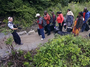 A Royal Canadian Mounted Police officer, left, standing in Saint-Bernard-de-Lacolle, Quebec, advises migrants that they are about to illegally cross from Champlain, N.Y., and will be arrested, Monday, Aug. 7, 2017.