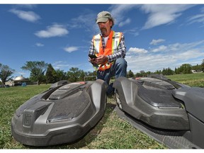 Maurice Pelletier, turf team leader park northwest, uses his phone to send commands to Edmonton's first electric, driverless lawn mowers that are going through a test run on a sports field in Coronation Park in Edmonton, June 27, 2018.