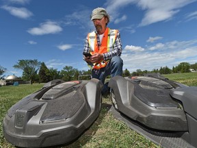 Maurice Pelletier, turf team leader park northwest, uses his phone to send commands to Edmonton's first electric, driverless lawn mowers that are going through a test run on a sports field in Coronation Park in Edmonton, June 27, 2018.