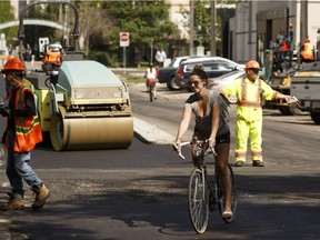 A cyclist rides past a construction crew repairing the bike lanes along 102 Avenue at 112 Street in Edmonton, on Friday, June 8, 2018. Work is being done along 102 Avenue from 111 Street to 121 Street.