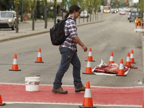 A pedestrian crosses as workers with Canadian Road Builders paint the sidewalk at 124 street and 109A Avenue to improve visibility in Edmonton, on Thursday, June 14, 2018. A second sidewalk at 124 Street and 110 Avenue was also painted.