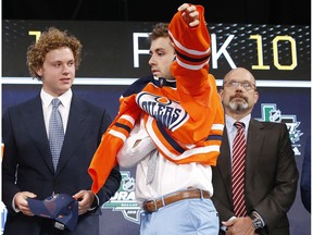 Evan Bouchard, centre, puts on a jersey after being selected by the Edmonton Oilers during the NHL hockey draft in Dallas, Friday, June 22, 2018.