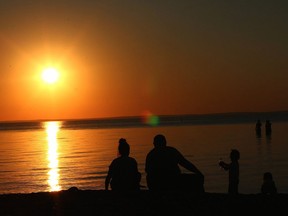 The sun sets behind people enjoying Ma-Me-O Beach on Pigeon Lake.