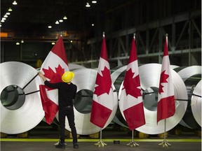 A worker straightens Canadian flags in front of rolls of coated steel before a visit by Foreign Affairs Minister Chrystia Freeland in Hamilton, Ont., on Friday, June 29, 2018. Freeland met with employees in the cold rolling plant and announced the government's latest efforts in response to U.S. tariffs on Canadian steel and aluminum.