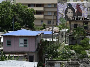 In this June 13, 2018 photo, houses affected by Hurricane Maria, some of them with their missing roofs covered in sturdy blue tarp, stand in the middle of the El Gandul neighborhood, in San Juan, Puerto Rico. There are thousands of people in similar circumstances across Puerto Rico nearly nine months since the most devastating storm to strike the island in decades.