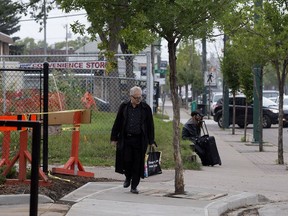 A pedestrian walks past a tree in the middle of the sidewalk along 107 Avenue west of 109 Street in Edmonton on Aug. 24, 2018.