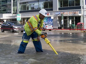 An Epcor worker inspects the area where the street flooded after a waterman break near the corner of 109 street and Jasper Avenue on Wednesday, Aug. 1, 2018 in Edmonton.