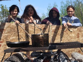 With dough wrapped around the tips of sticks, students fry bannock while moose meat stew cooks over a fire. The students are part of the experiential learning Initiative program held by the Northland School Division No. 61 outside Father R. Perin School in Janvier, Alta. on May 15, 2018.