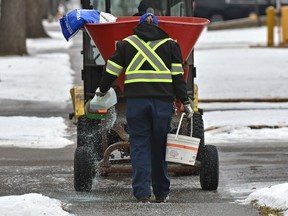 A worker follows behind a salt spreader filling in the gaps misses along the 112 St. downtown sidewalks after freezing rain fell during the morning in Edmonton, November 9, 2018.