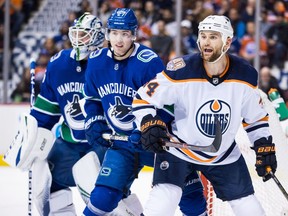 Edmonton Oilers forward Zack Kassian, right, holds Vancouver Canucks defenceman Ben Hutton's stick as they battle for position in front of goalie Jacob Markstrom during NHL action in Vancouver on Dec. 16, 2018.