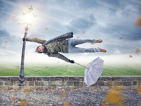 Man flying away horizontally in a storm while holding on to a street lamp with one hand. The other hand is holding an upended umbrella.